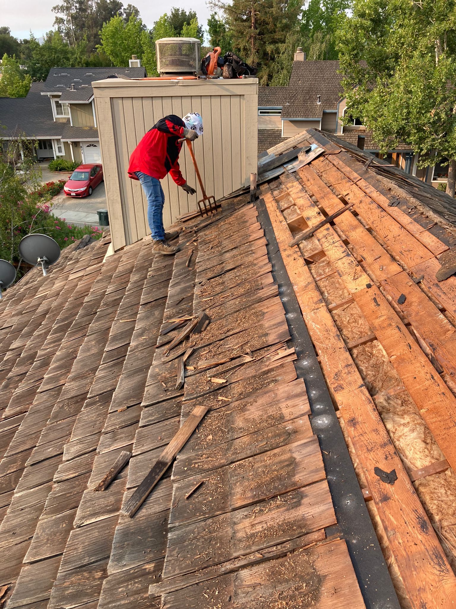 how much does it cost to repair a roof leak. Image of man standing on old shingle roof removing peices.